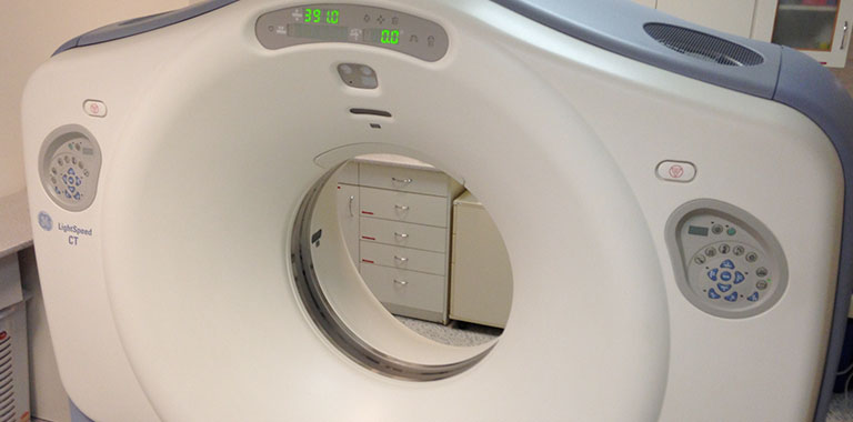 Ausschnitt eines Kernspintomographen. Im Hintergrund erkennt man weiße Schränke.