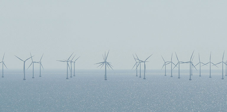 [Translate to en:] Ausschnitt eines Offshore Windparks. Zu sehen sind ca. 20 Windkrafträder. Das Wetter ist eher diesig und das Meer ist ruhig.