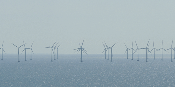 Ausschnitt eines Offshore Windparks. Zu sehen sind ca. 20 Windkrafträder. Das Wetter ist eher diesig und das Meer ist ruhig.